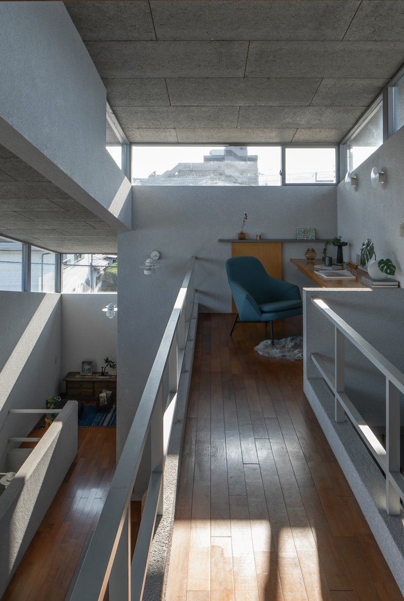 Upper-level hallway overlooking split-level interior spaces with exposed concrete ceiling and angular clerestory windows