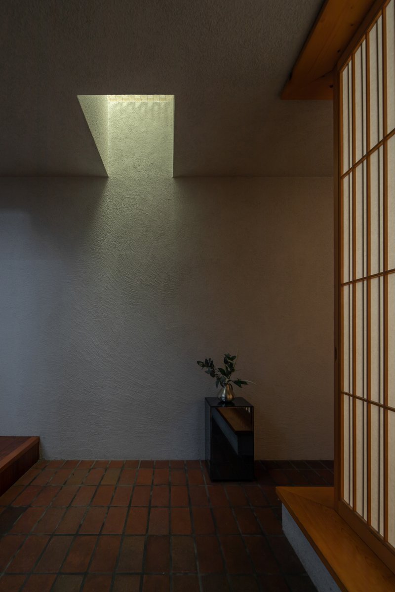 Entry hall with trapezoidal skylight casting geometric shadows on textured plaster wall beside wooden screen door