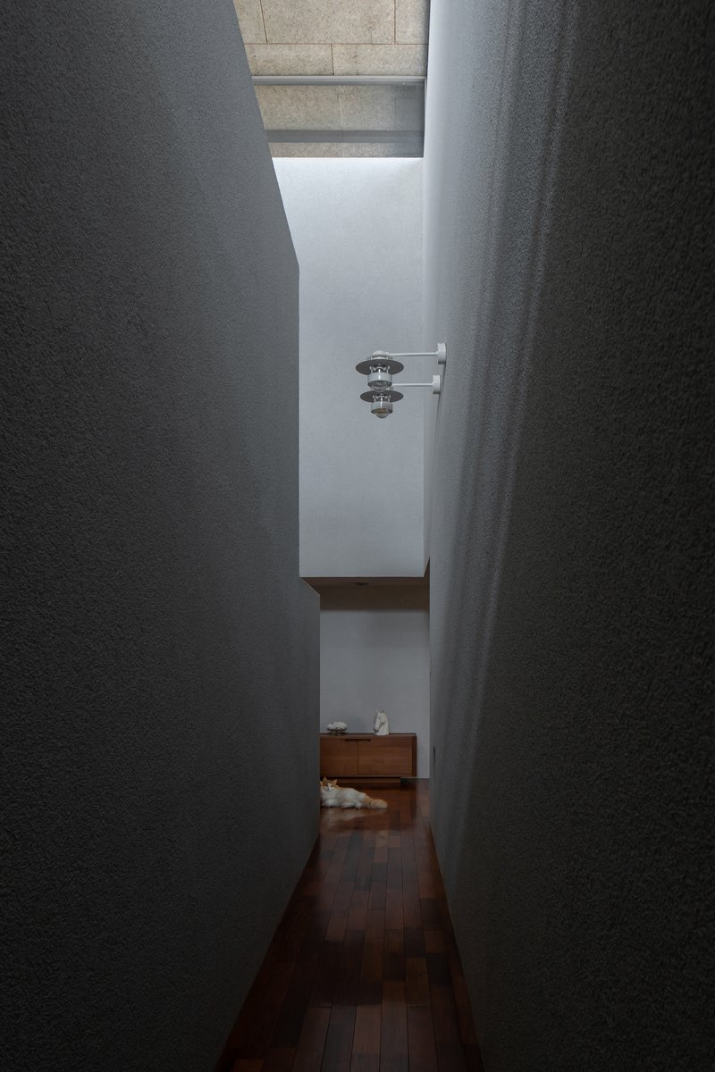 Narrow corridor with textured plaster walls opening to a skylit space beyond