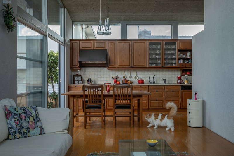Open kitchen with timber cabinetry and dining table beneath exposed concrete ceiling and clerestory windows