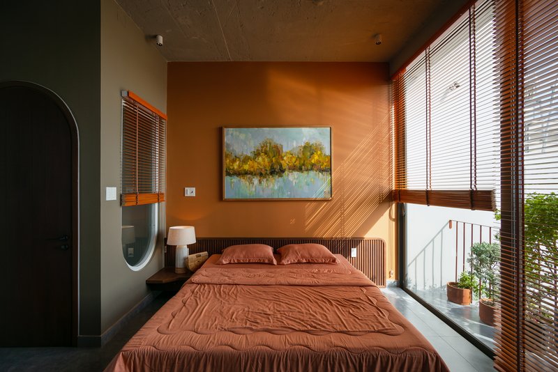 Bedroom with terracotta walls and horizontal wood blinds beneath an exposed concrete ceiling at dusk