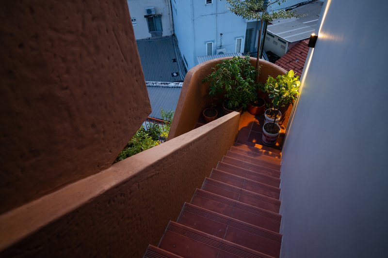 Rooftop stair with textured red tile treads descending between planted beds at evening