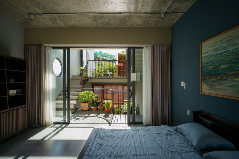 Bedroom with exposed concrete ceiling opening through glass doors to a planted terrace with morning light