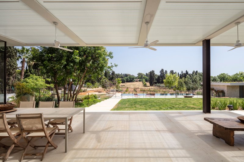 Covered terrace with slatted ceiling and ceiling fans opening onto lawn and pool beyond mature trees