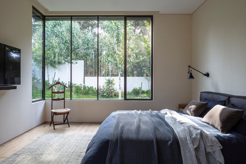Bedroom with corner window framing a white-walled garden courtyard planted with shrubs and small trees