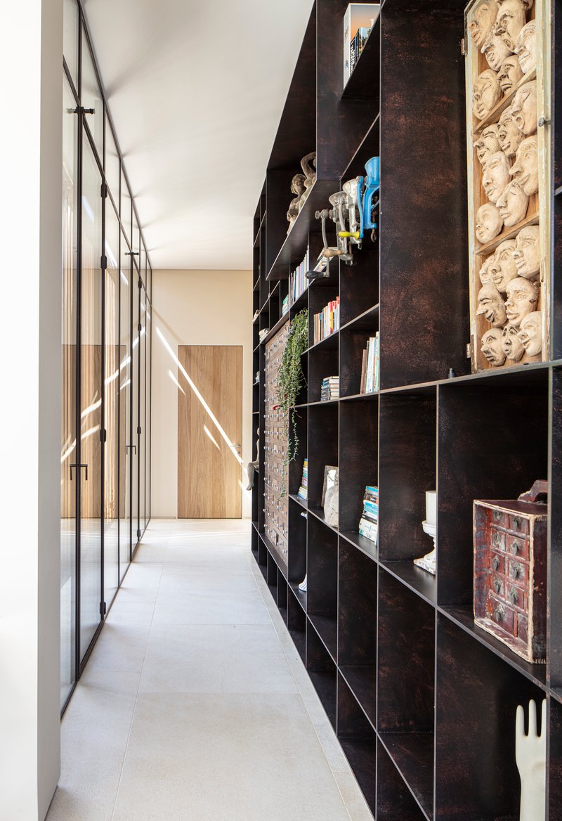 Narrow corridor with dark metal shelving along one side and steel-framed glazing on the other