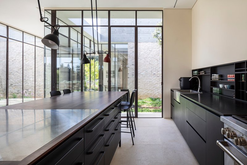 Kitchen with island and black cabinetry opening to a planted courtyard through steel-framed glass doors