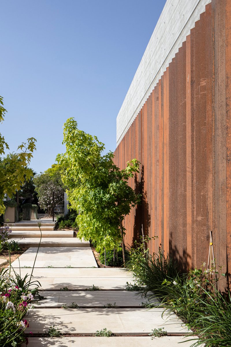 Weathered steel vertical cladding alongside a stepping stone path edged with planted beds