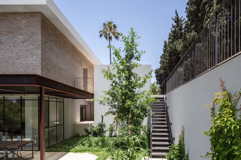 Courtyard with exterior staircase against white wall and planted beds beside the glazed ground floor