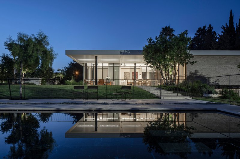 Glass pavilion with flat roof reflected in a still pool at dusk
