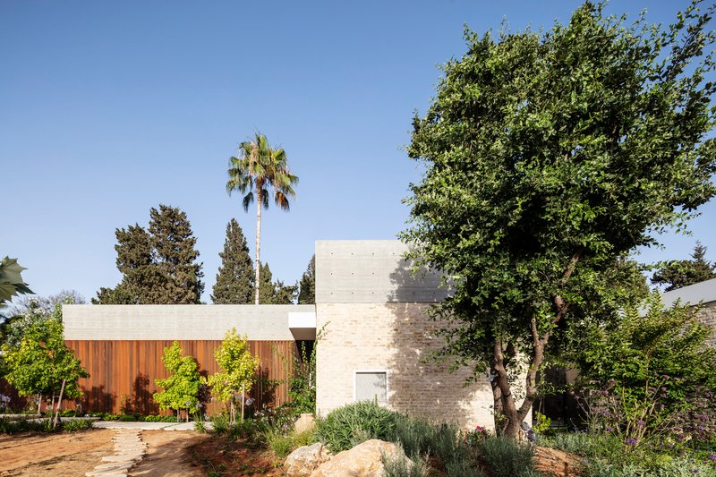 Board-formed concrete volumes with timber slat screening behind planted beds and mature trees
