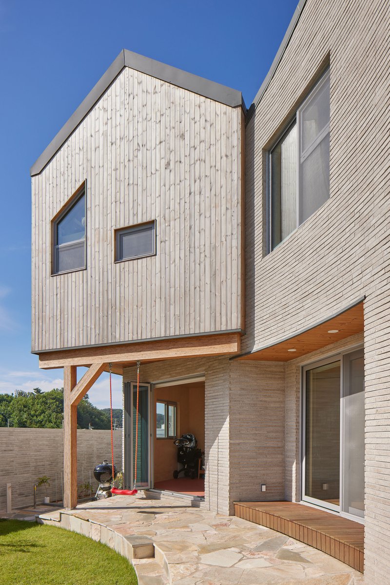 Cantilevered timber volume on exposed brackets above a stone terrace and lawn under blue sky