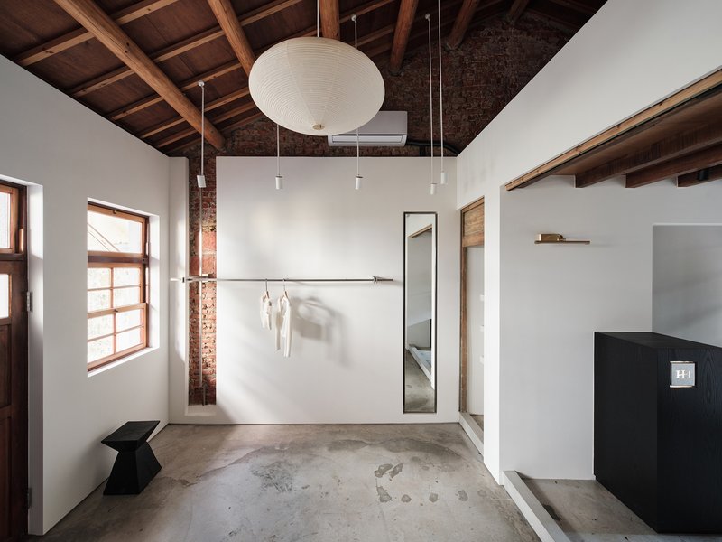 Retail room with concrete floor, exposed brick column, and wall-mounted clothing rail casting soft shadows