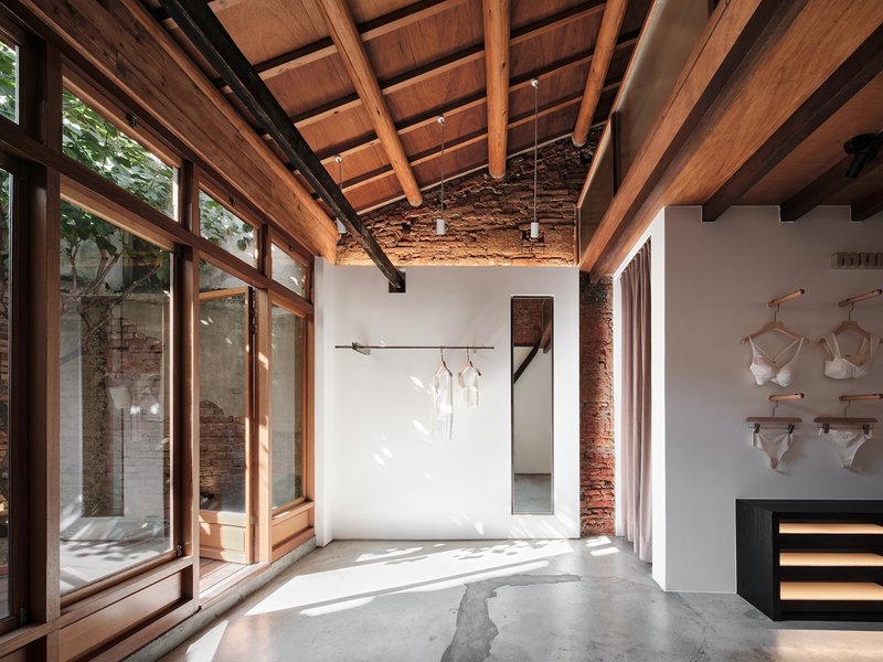 Interior room with timber-framed glazing overlooking courtyard, concrete floor, and dappled afternoon light