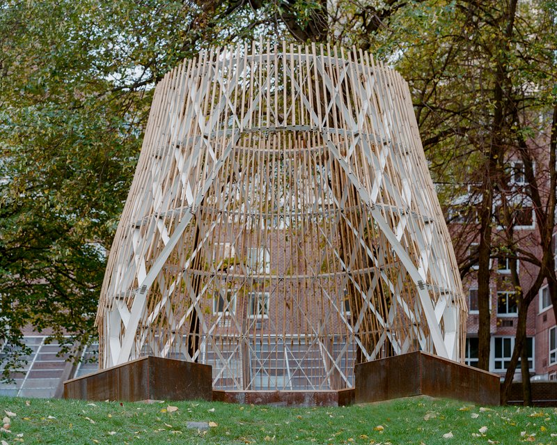 Close view of the lattice pavilion facade showing diagonal timber members and vertical slats against brick buildings