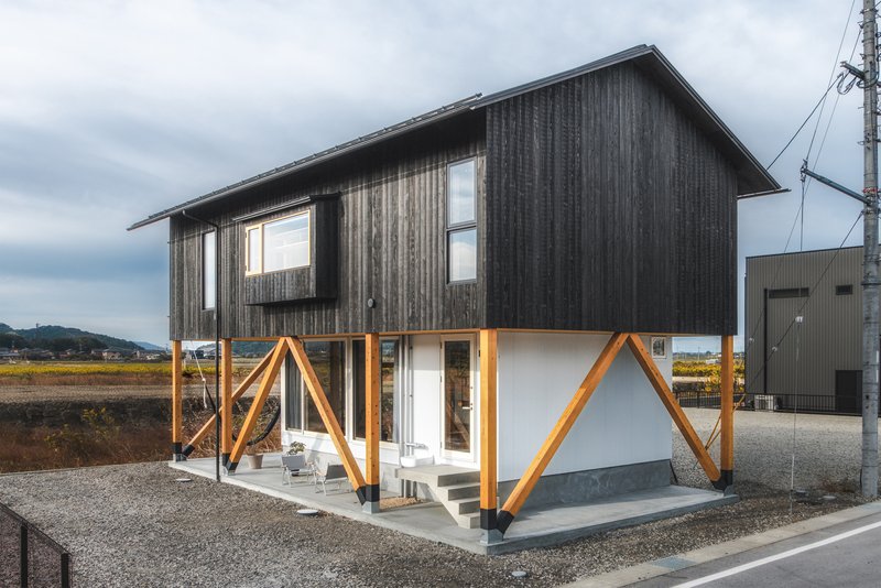 Exterior view showing charred timber cladding above white stucco with diagonal timber bracing at ground level