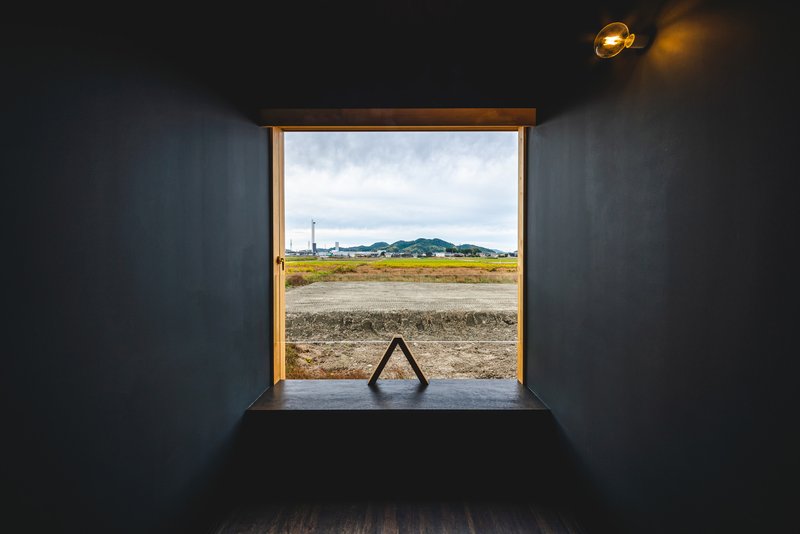 Timber-framed window opening onto fields and distant hills from a dark-walled interior at dusk