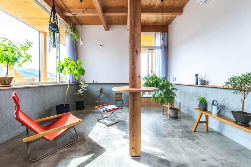 Concrete floor living space with timber columns, zinc wainscoting, and potted plants by windows