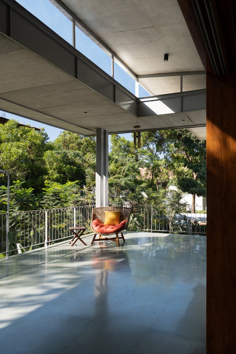 Covered balcony with polished concrete floor and an orange leather chair facing dense green trees