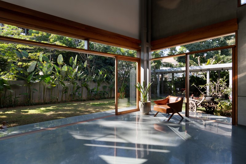 Glass-walled interior space with timber frames opening onto a grassed courtyard with banana plants