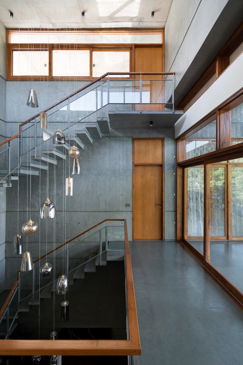 Double-height stairwell with concrete walls, glass balustrade, and suspended pendant lights over the void