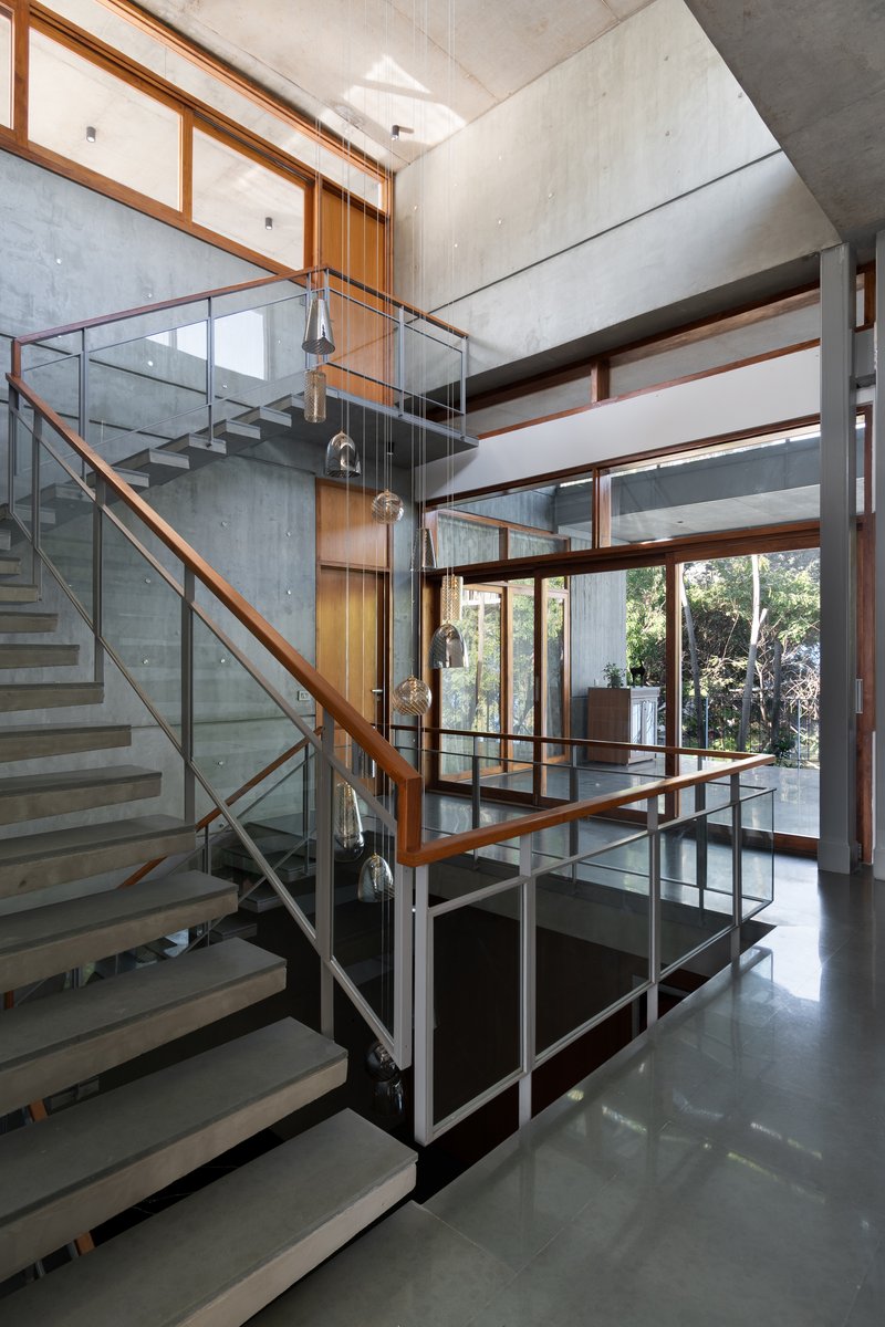 Central staircase with glass and timber railings linking split levels beneath exposed concrete ceilings