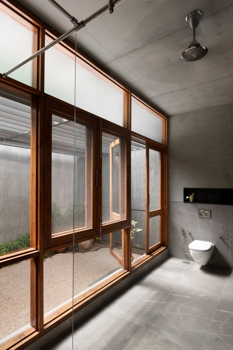 Bathroom with exposed concrete ceiling and timber-framed glazing opening to a small gravel courtyard