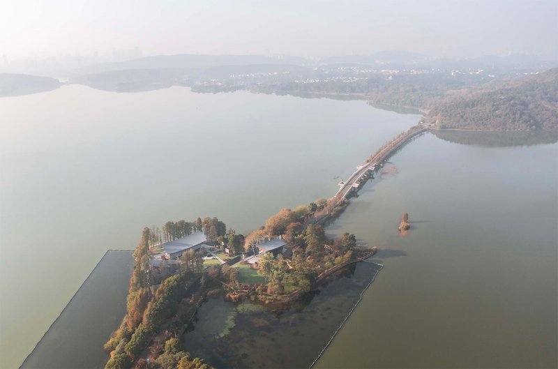 Aerial view of lakeside peninsula with buildings connected by causeway through misty water