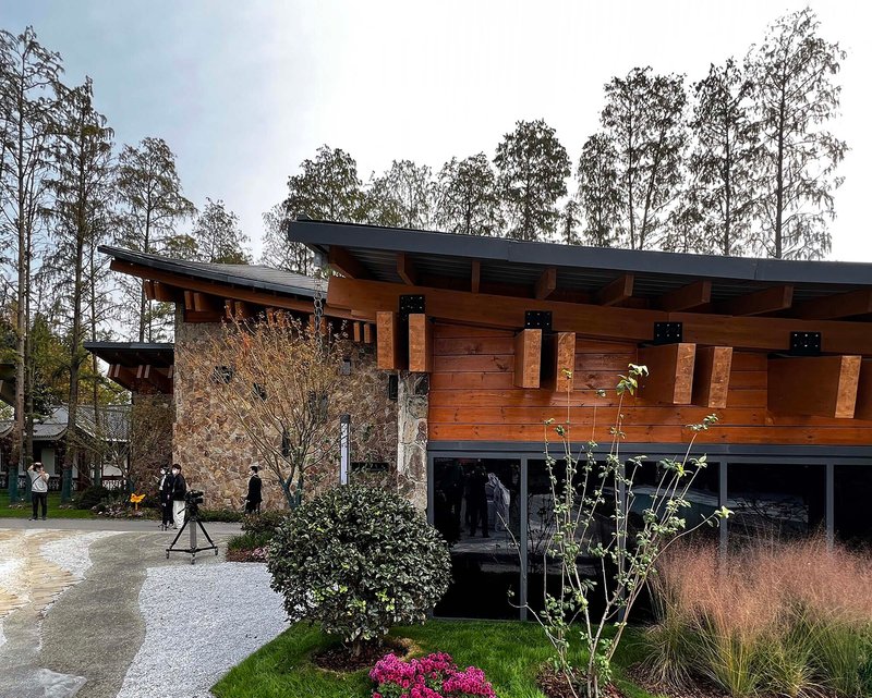 Timber cladding and exposed joinery detail of the overhanging roof with visitors and flowering shrubs below in dusk light