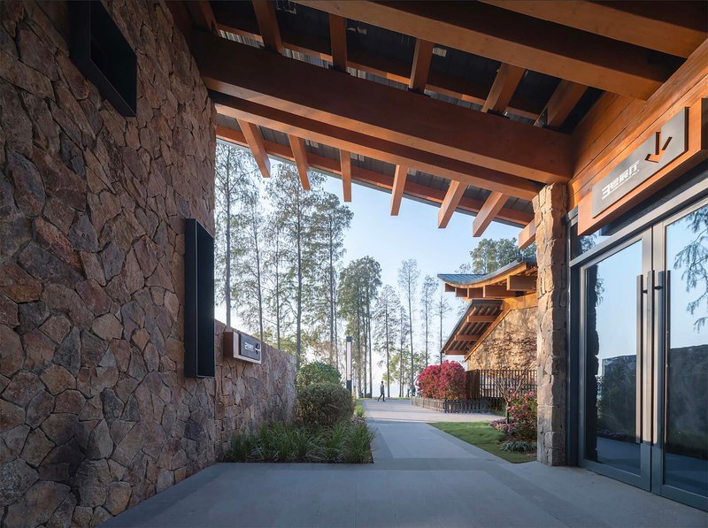 Covered walkway framed by stone walls and timber beams opening onto a path with distant figures beneath bare trees