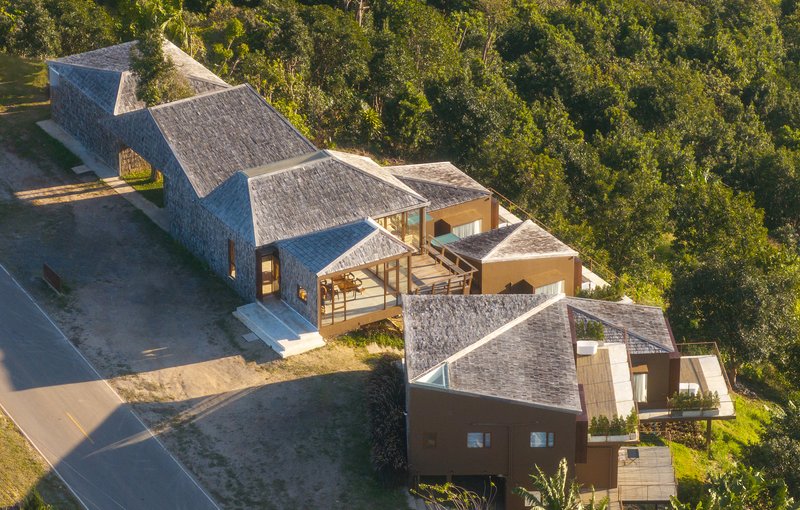Aerial view of the compound with multiple peaked roofs scattered among green lawn and wooded edges