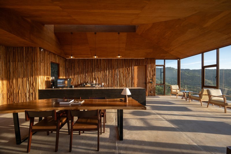 Open dining and kitchen space with vertical timber slat wall and pendant lights casting shadows on concrete floor