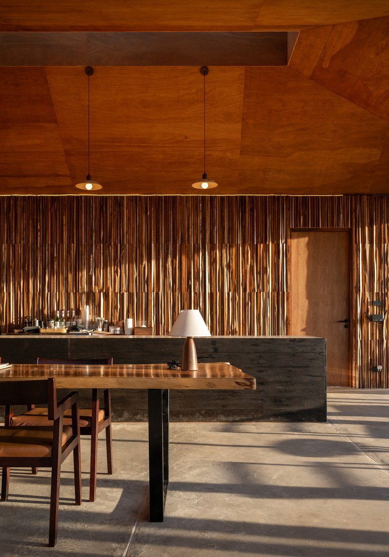 Kitchen island with dark stone base and timber dining table under warm pendant lights and geometric wood ceiling