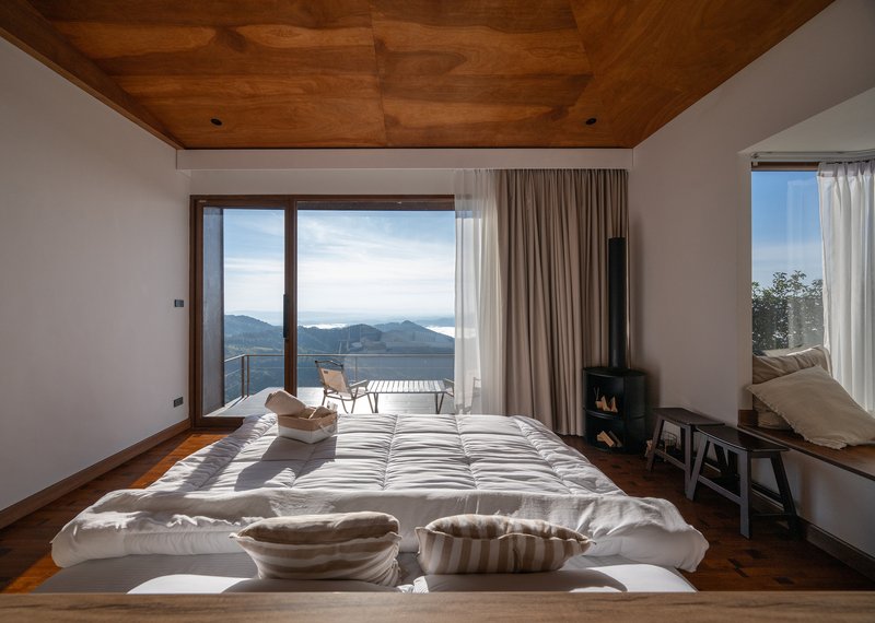 Bedroom with low platform bed and black woodstove looking toward mountain vista through open glass doors