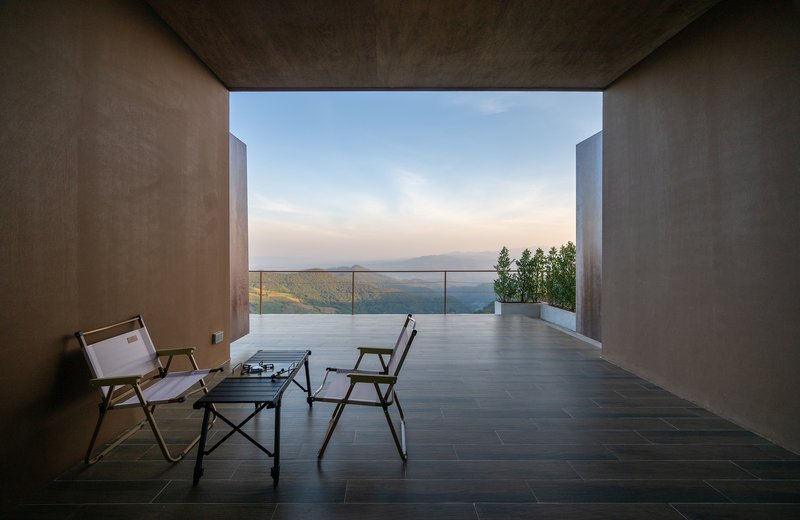 Covered terrace with dark stone flooring and two chairs overlooking rolling mountains through a wide opening