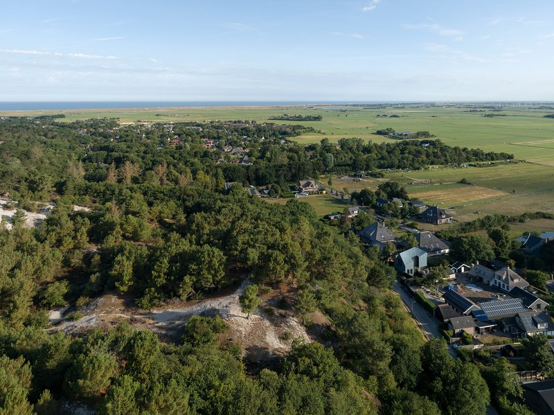 Drone view of the settlement bordered by wooded areas and adjacent farmland under clear skies