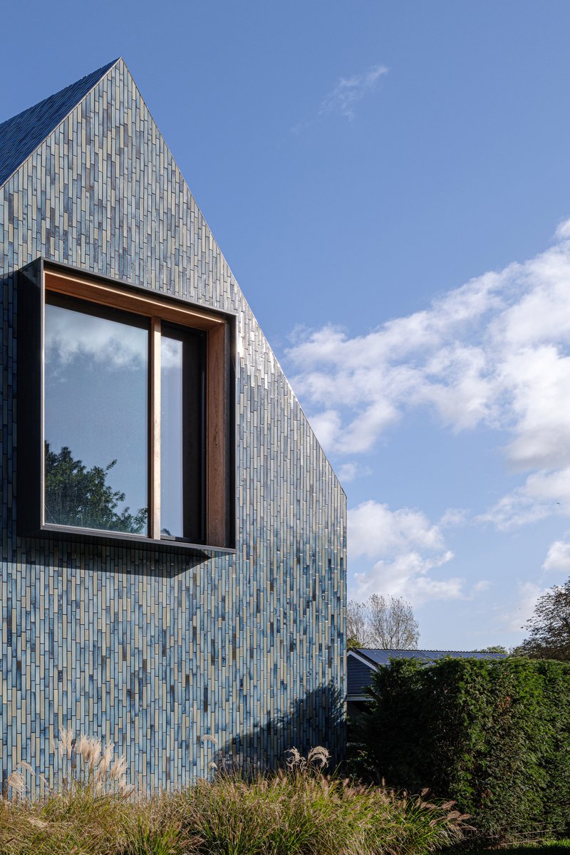 Projecting timber-framed window box set within the glazed tile facade under scattered clouds