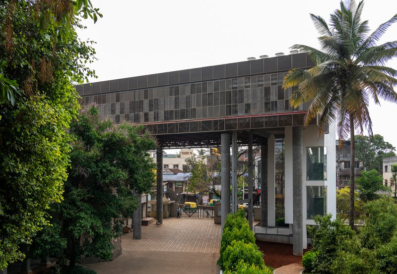 Elevated volume on pilotis framing a paved courtyard with palm trees and surrounding greenery