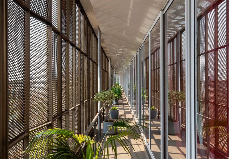 Corridor lined with perforated metal screens and potted plants casting dappled shadows along the floor