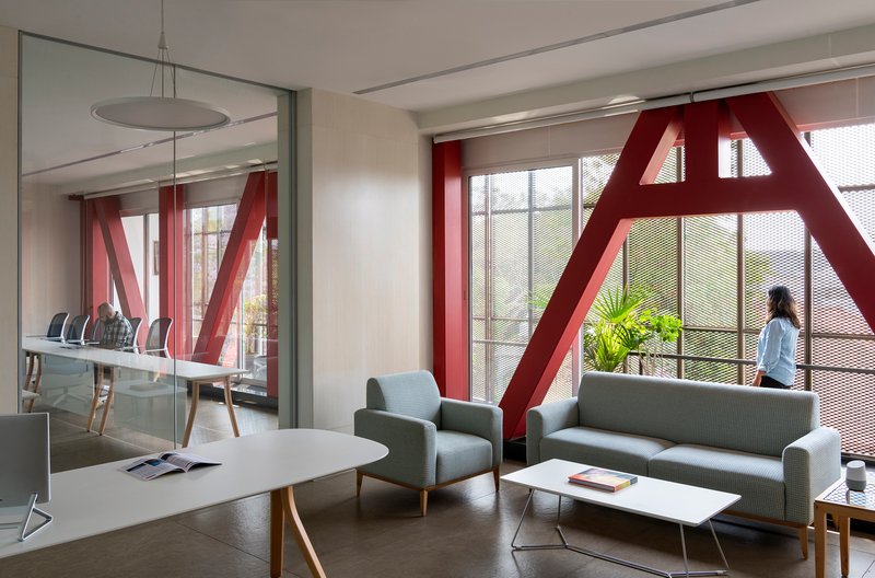 Lounge area with red diagonal steel bracing at glazed facade and a person standing by window