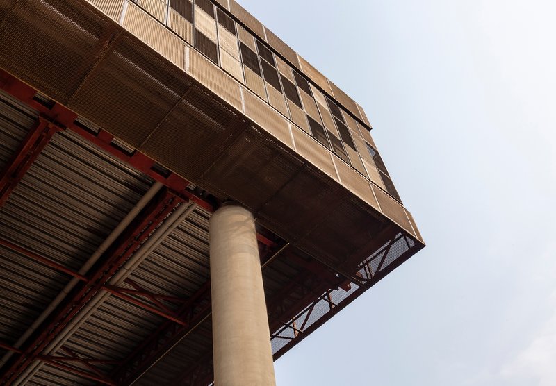 Upward view of cantilevered volume with exposed red steel trusses and concrete column