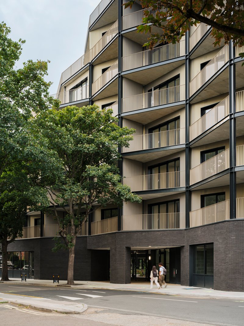 Facade detail showing vertically slatted balcony screens and dark brick base with pedestrians passing by