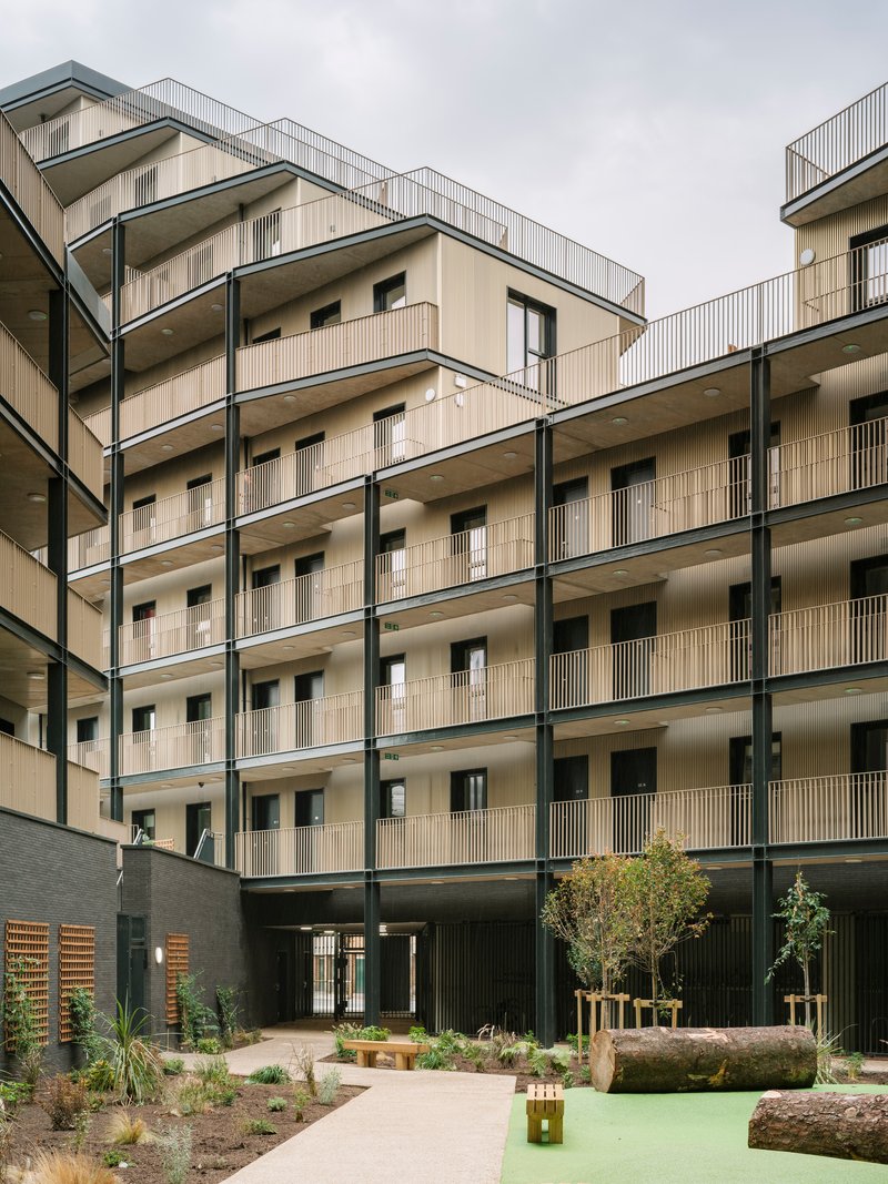 Shared courtyard with planted beds, young trees, and pale facades framing the communal space