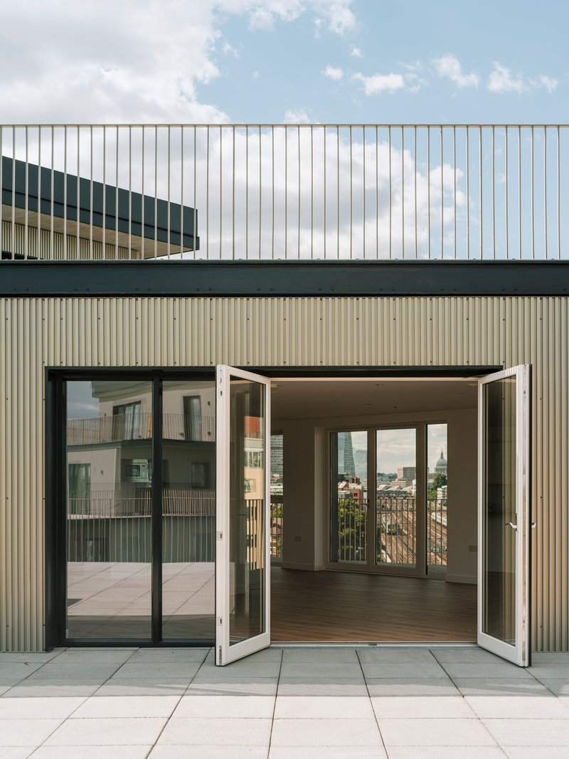 Rooftop terrace with open folding glass doors leading into an apartment under a partly cloudy sky
