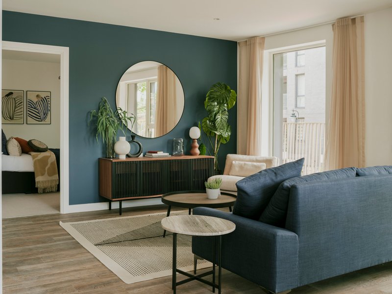 Living room with dark teal accent wall, circular mirror above a credenza, and potted plants by the window