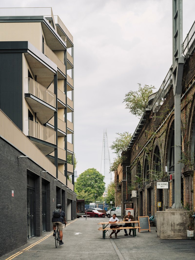 Street view showing the residential facade with alternating balconies and a cyclist passing nearby