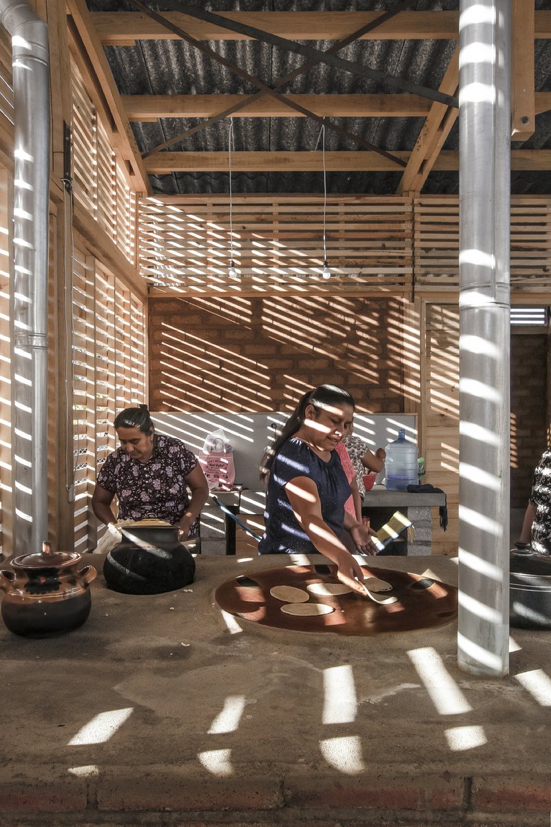 Striped sunlight patterns cast through horizontal timber slats onto the polished concrete floor and metal flue