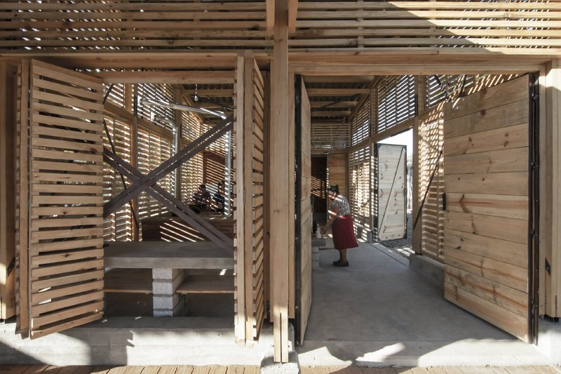 Interior threshold with diagonal timber bracing and slatted walls filtering dappled sunlight