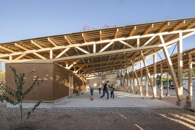 Covered outdoor space with white-painted diagonal timber trusses and children playing beneath