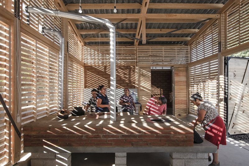 Raised brick platform with horizontal slatted timber screens filtering afternoon light onto seated children